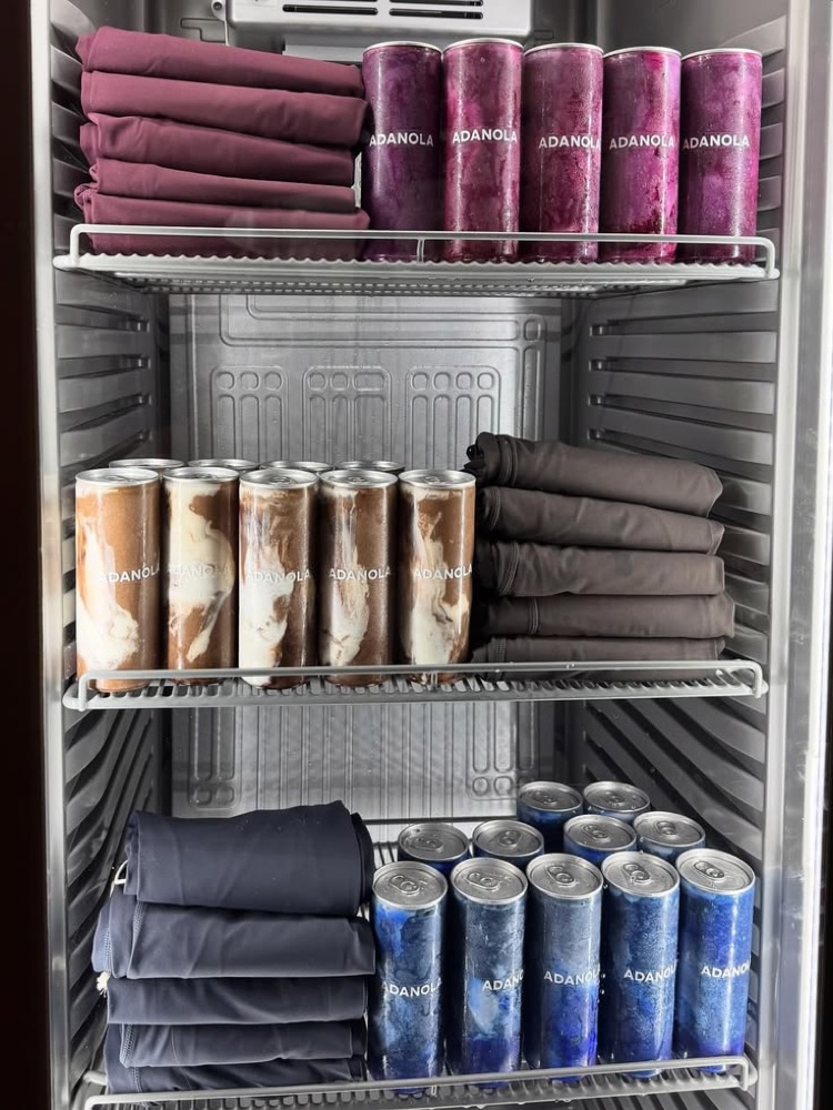 A gym fridge stocked with the gym's own branded protein shakes next to apparel