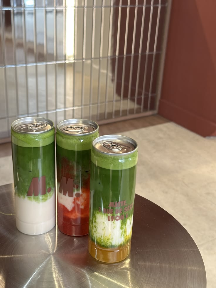 Three colourful branded cans of matcha, strawberry and orange