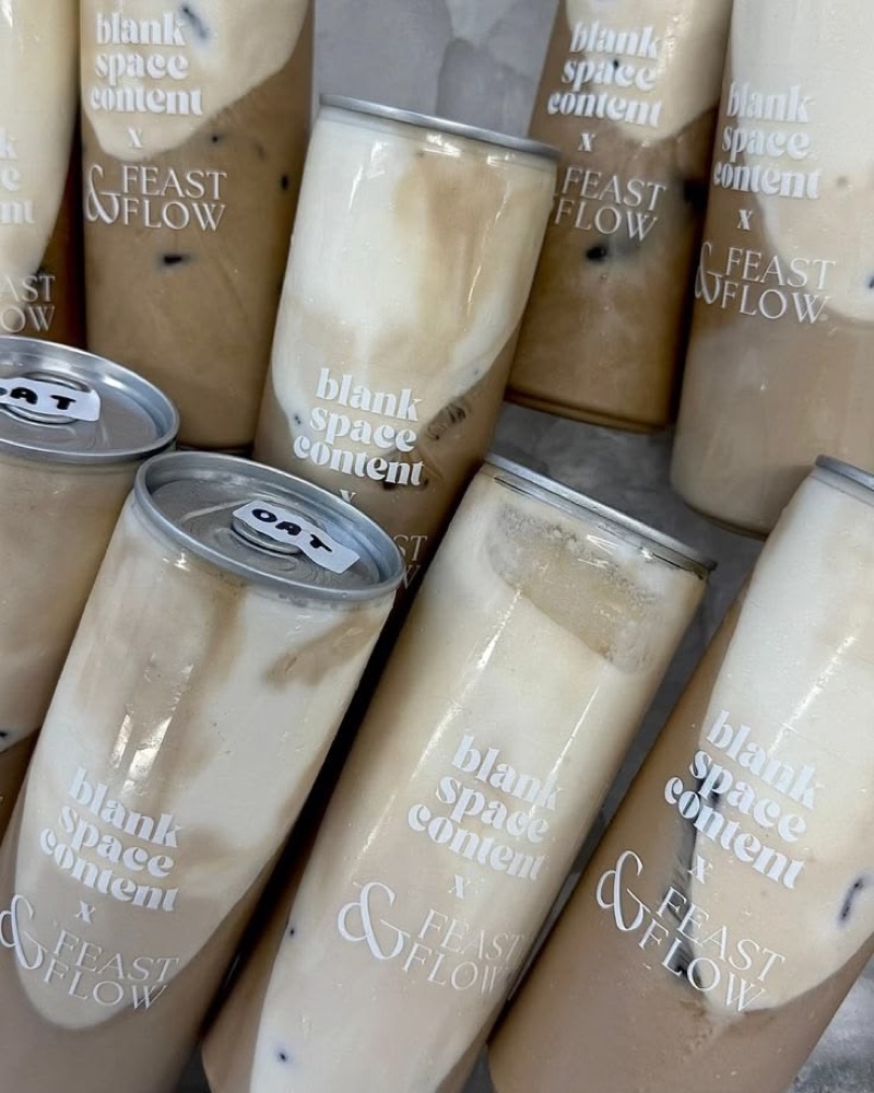 A pile of oat latte cans printed with a coffee shop's own branding