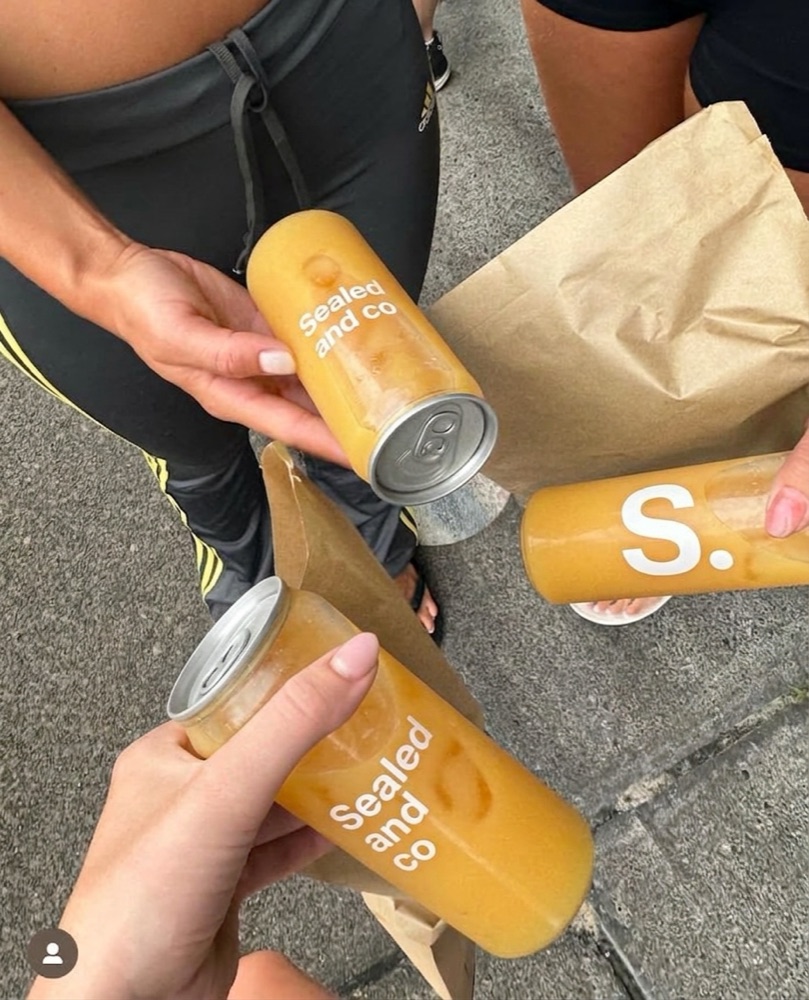 Three friends cheersing sealed and co orange juice cans